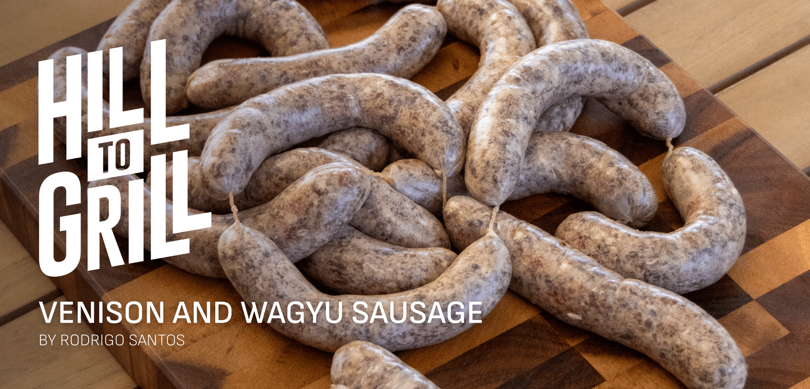 Venison and Wagyu sausages on a wooden cutting board with 'Hill to Grill' branding.